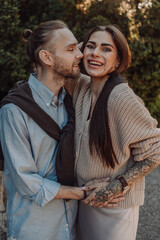 Smiling tattooed girl hugging her boyfriend in a park. Pretty redhead woman with tattoos and man on a walk.