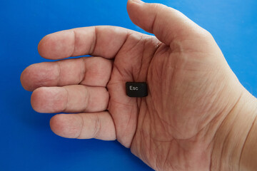 Escape key in the palm of a man's hand on a blue background, end of project, one way out, only solution, no alternative