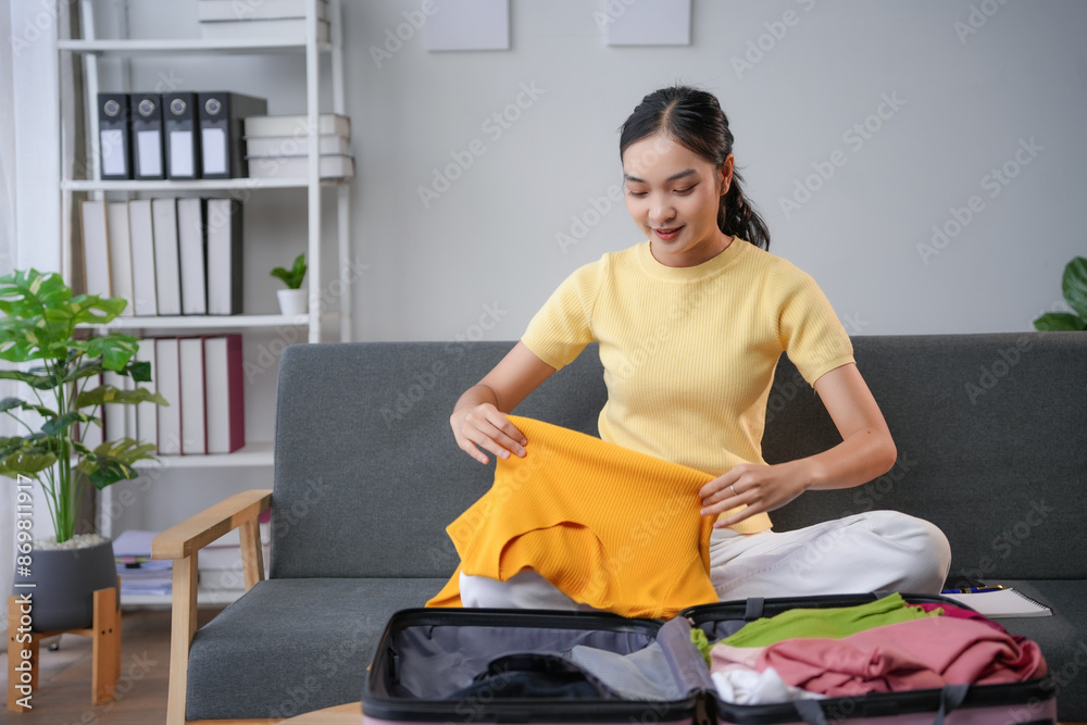 Wall mural Young woman packing clothes for trip at home