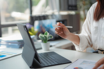 Businesswoman analyzing charts on tablet and taking notes with stylus in modern office