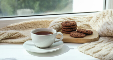 Beige knitted scarf, tea and cookies on windowsill