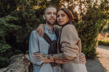 Fototapeta premium Smiling tattooed girl hugging her boyfriend in a park. Pretty redhead woman with tattoos and man on a walk.