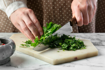 Woman cutting fresh coriander at white marble table, closeup