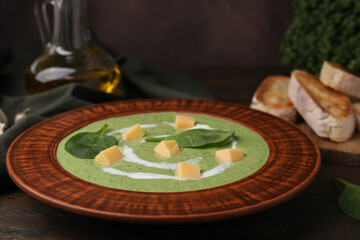 Delicious spinach cream soup with leaves and cheese in bowl on wooden table, closeup