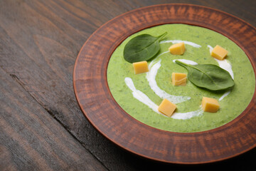 Delicious spinach cream soup with leaves and cheese in bowl on wooden table, closeup. Space for text