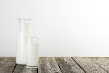 Carafe and glass of fresh milk on wooden table, space for text