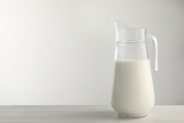 Glass jug with fresh milk on light wooden table. Space for text