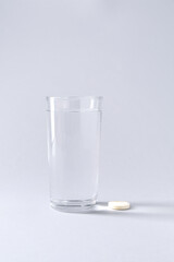 Effervescent pill and glass of water on light grey background