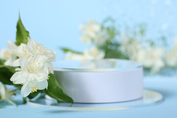 Presentation of product. White podium and beautiful jasmine flowers on light blue background closeup