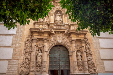 Obraz premium Detail of the ornate and baroque facade of the La Merced church in Murcia, Spain, between two orange trees