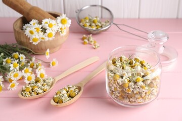 Dry and fresh chamomile flowers in dishware on pink wooden table