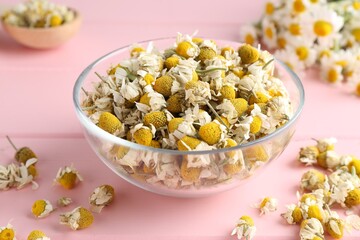 Chamomile flowers in glass bowl on pink wooden table, closeup