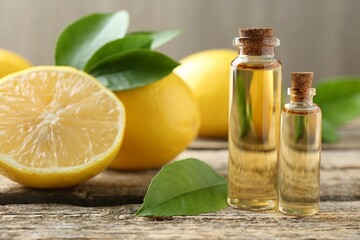Essential oils in bottles, lemons and green leaves on wooden table, closeup