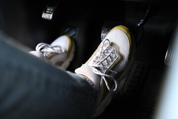 Woman in sneakers pushing on pedal of car brake, closeup