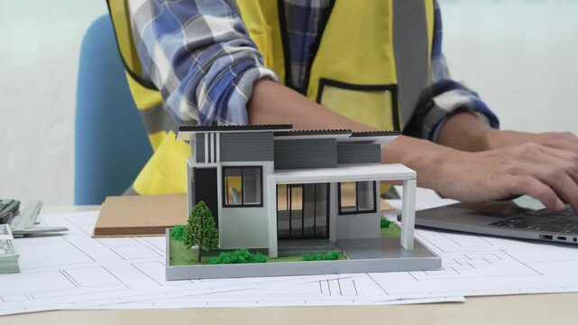 Professional architect team and engineer discuss about architectural project on meeting table with safety helmet, wooden block and architectural document scatter around. Closeup. Delineation.
