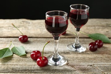 Glasses of delicious cherry liqueur and juicy berries on wooden table