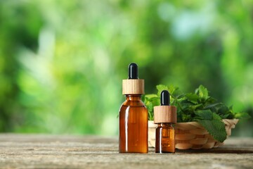 Bottles of mint essential oil and fresh leaves on wooden table, space for text