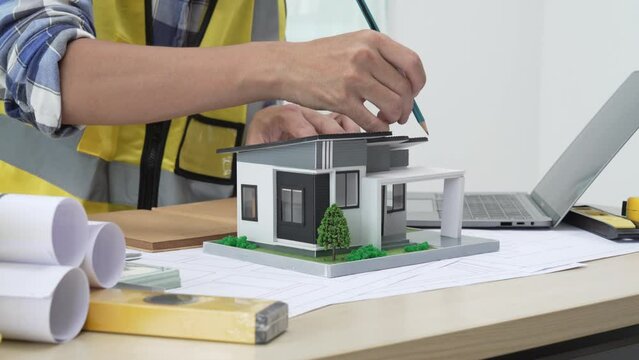 Professional architect team and engineer discuss about architectural project on meeting table with safety helmet, wooden block and architectural document scatter around. Closeup. Delineation.