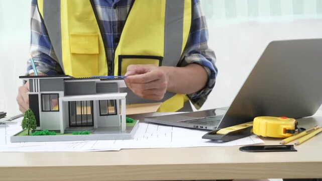 Professional architect team and engineer discuss about architectural project on meeting table with safety helmet, wooden block and architectural document scatter around. Closeup. Delineation.