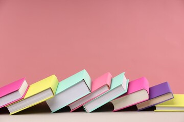 Many colorful books on beige table against pink background, space for text