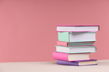 Stack of colorful books on beige table against pink background, space for text