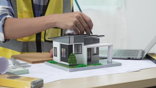 Professional architect team and engineer discuss about architectural project on meeting table with safety helmet, wooden block and architectural document scatter around. Closeup. Delineation.