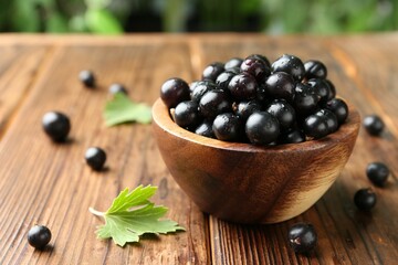 Ripe black currants and leaves in bowl on wooden table, closeup. Space for text