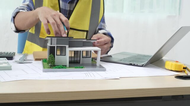 Professional architect team and engineer discuss about architectural project on meeting table with safety helmet, wooden block and architectural document scatter around. Closeup. Delineation.