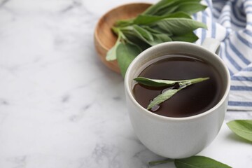 Aromatic herbal tea in cup with sage on white marble table, space for text