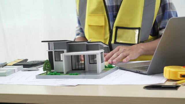 Professional architect team and engineer discuss about architectural project on meeting table with safety helmet, wooden block and architectural document scatter around. Closeup. Delineation.