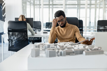 Dark-skinned young architect working in the office and looking tired