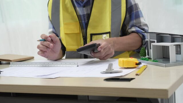 Professional architect team and engineer discuss about architectural project on meeting table with safety helmet, wooden block and architectural document scatter around. Closeup. Delineation.