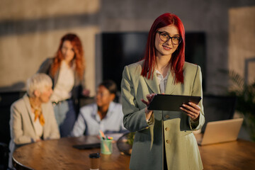 Happy female manager with tablet looking at camera during the meeting.