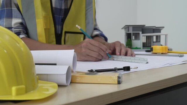 Professional architect team and engineer discuss about architectural project on meeting table with safety helmet, wooden block and architectural document scatter around. Closeup. Delineation.