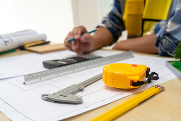Professional team of architects and engineers discuss architectural project on conference table with hard hats, wooden blocks and architectural documents scattered around. Close-up. Drawing.