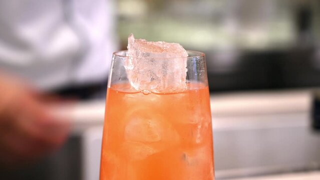 Bartender prepares orange cocktail with ice cubes in bar setting. Close-up shot of drink preparation