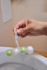 Gently placing a toilet bowl cleaning tablet containing floating balls with your hand