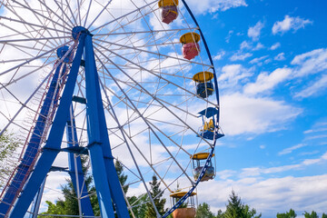 Big ferris wheel in an amusement park, against the background of the blue sky with clouds. Rest, vacation, emotions, joy.