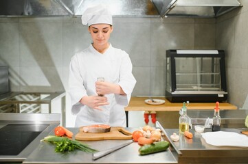 young beautiful female chef cooks salmon in restaurant kitchen