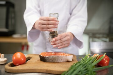 young beautiful female chef cooks salmon in restaurant kitchen