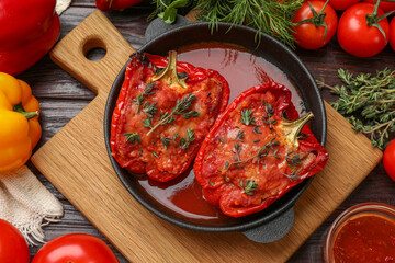 Tasty stuffed peppers in dish and ingredients on wooden table, flat lay