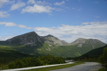  Mountains and nature of Norway. Summer and sunny day. Green valley and white clouds. Blue sky. Snow on the slopes of the mountains.