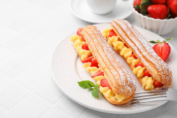 Delicious eclairs filled with cream, strawberries and mint on white tiled table, closeup. Space for text