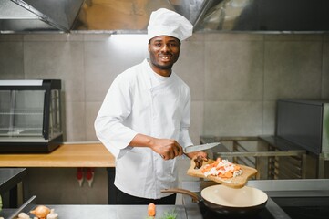 Portrait of happy African American male chef standing in restaurant kitchen