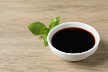 Balsamic vinegar and basil on light wooden table, space for text