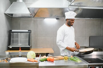 Experienced professional African-American chef standing in kitchen of restaurant with working staff