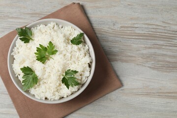 Tasty cooked rice with parsley in bowl on wooden table, top view. Space for text