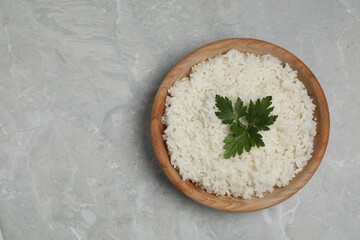 Tasty cooked rice with parsley in bowl on grey marble table, top view. Space for text