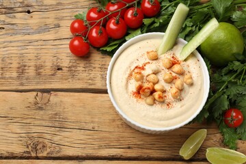 Tasty hummus with chickpeas in bowl and fresh products on wooden table, flat lay. Space for text