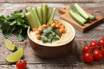 Tasty hummus with chickpeas in bowl and fresh products on wooden table, closeup